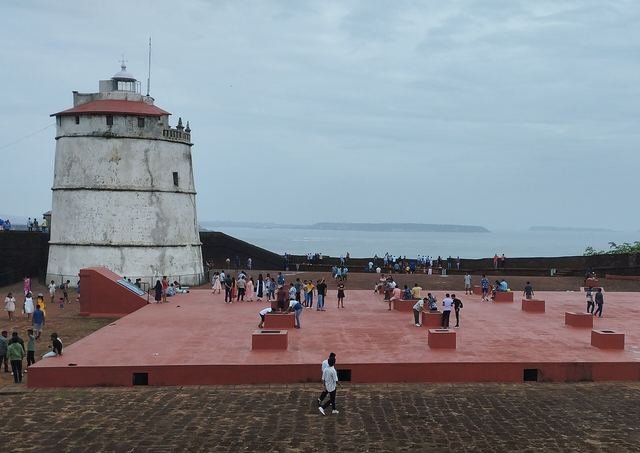 The white lighthouse at Fort Aguada with visitors on the fort's open terrace and the Arabian Sea behind