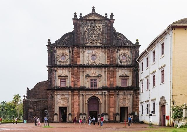 The carved laterite front of the Basilica of Bom Jesus in Old Goa, with visitors in the courtyard
