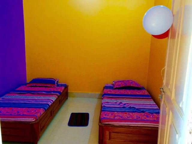 A simple room with yellow and purple walls, two single beds with striped covers and a small floor mat