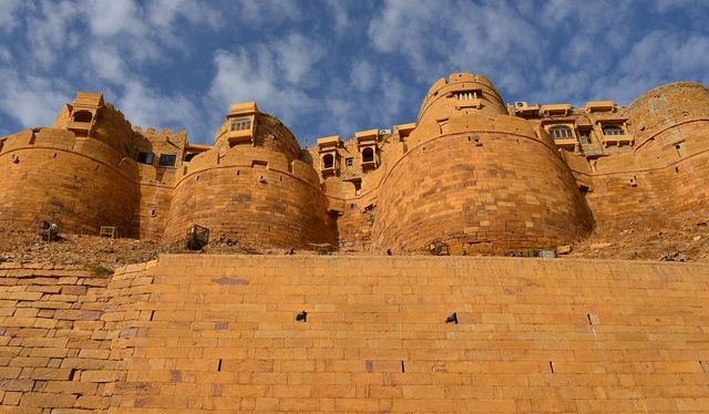 Rounded golden sandstone bastions of Jaisalmer Fort against a blue sky with clouds