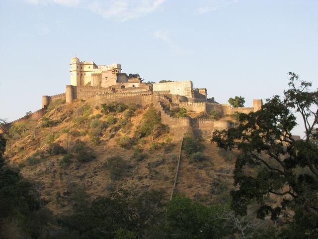 Kumbhalgarh Fort's palace buildings on top of a scrub-covered hill in warm evening light